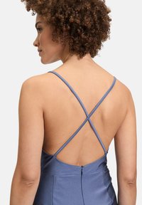 Blauwe jurk met kruislings gespen en een open rug. Glad textuur en subtiele glans. Ritsdetail op de rug ter hoogte van de taille.