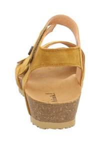 Gelbe Wildledersandalen mit Korksohle, offenem Rücken und einem verstellbaren Riemen. Sie haben eine abgerundete Zehenpartie und ein strukturiertes Fußbett.