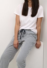 T-shirt blanc associé à un pantalon rayé bleu et blanc avec une taille à cordon de serrage et deux poches latérales. Texture de tissu lisse.