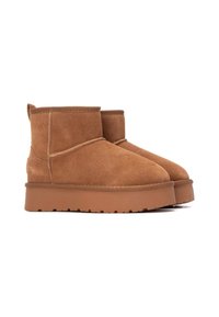 Botas de ante marrón hasta el tobillo con punteras redondeadas, detalles de costura mínimos y una suela de goma gruesa con un patrón de textura.