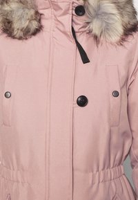 Rosa parka med en huva i fuskpäls, med tryckknappar, sidofickor och ett elastiskt midjeband för en figurnära look. Slät tygtextur.