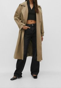 Beżowy trench coat na czarnym topie crop, w połączeniu z czarnymi dżinsami w wysokim stanie. Lśniące czarne loafersy dopełniają stylizację.