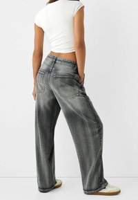 Szerokie dżinsy o luźnym kroju wykonane z wyblakłego szarego denimu, z dwoma tylnymi kieszeniami i delikatnie postarzanym wyglądem. Połączone z białym obuwiem.