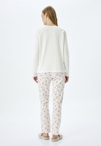 Long-sleeve cream top with a rounded neckline, paired with light pink pants patterned with croissants and cups, worn with beige slippers.