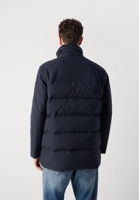 Giacca a vento blu navy con colletto alto, design trapuntato e finitura opaca elegante. Caratterizzata da una vestibilità rilassata e un orlo dritto.