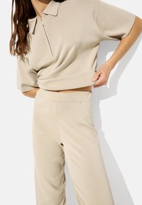 Beżowy sweter polo z pół zamkiem i krótkimi rękawami, w parze z dopasowanymi spodniami o wysokim stanie. Gładka faktura i minimalistyczny design.