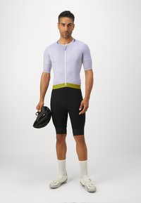 Maillot de cyclisme violet clair à manches courtes avec une fermeture éclair à l'avant, associé à un cuissard de cyclisme noir et un casque noir.