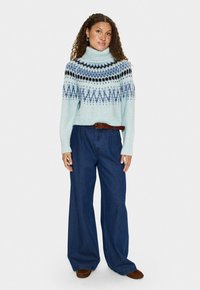 Heled sinine kootud sveter kõrge kraega, mis on kaunistatud geomeetriliste mustritega tumesinises ja mustas. Kombineeritud avara jalgadega tumedate teksadega.
