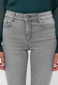 Jeans in denim grigio con vita alta, dotati di chiusura a bottoni frontale, passanti per cintura e design a cinque tasche. Tessuto liscio, con una leggera scoloritura minima.