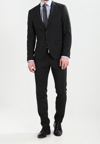 Ullblandad skräddarsydd kostym i mörkgrått, med en en-knappskavaj, slim-fit byxor och en ljusblå skjorta med en grå slip. Svarta läderskor.