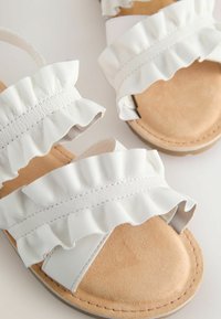 Witte sandalen met rimpelige banden, van leer, met een platte tan kleurige zool en een minimalistisch ontwerp. Zachte textuur en subtiele stikdetails.