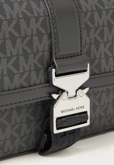 Sac à motif noir avec monogramme MK, doté d'un fermoir argenté avec le nom de la marque, d'accents en cuir et d'une finition en tissu texturé.