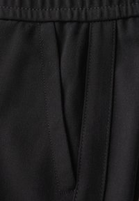 Gros plan sur une poche en tissu noir avec des coutures visibles et une ceinture froncée au-dessus de la poche.