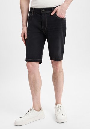 Schwarze Denim-Shorts mit heller Naht, vorderen Taschen und klassischem Schnitt. Kombiniert mit einem figurbetonten weißen Oberteil und weißen Sneakers.