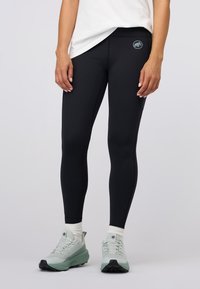 Czarne legginsy wykonane z elastycznego materiału, z małym logo na talii. Połączone z jasnoszarymi butami turystycznymi.