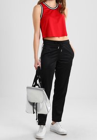 Röd kort topp med svart krage, kombinerad med svarta träningsbyxor med sidostreifen och dragsko. Silverfärgad ryggsäck och vita sneakers.