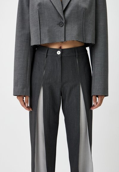 Gray cropped blazer with button closure and frayed hem, paired with gray pants featuring sheer side panels and a front button.