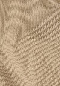 Tela texturizada beige con un fino patrón de costilla diagonal, que muestra una superficie suave y ligeramente elástica.