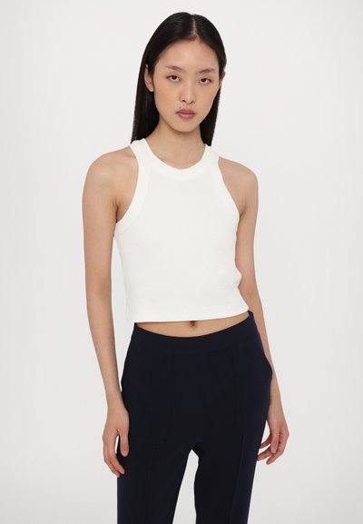 Weißes geripptes Crop-Top mit hohem Hals und ärmellosem Design, kombiniert mit marineblauen Hosen mit Fronttaschen und lockerer Passform.