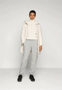 Puffjakke i off-white med høj krave, parret med en lys beige sweatshirt og grå sweatpants. Sorte sneakers fuldender outfittet.