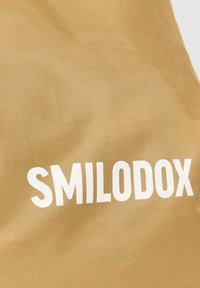 Borsa in tessuto dorato con una superficie testurizzata che presenta un grande logo bianco "SMILODOX". Il design sottolinea la durata e la funzionalità.