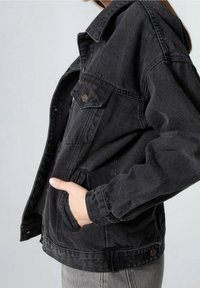Giacca di jeans nera con un design strutturato, chiusura frontale con bottoni, tasca sul petto e tasche laterali, caratterizzata da una texture leggermente sbiadita.