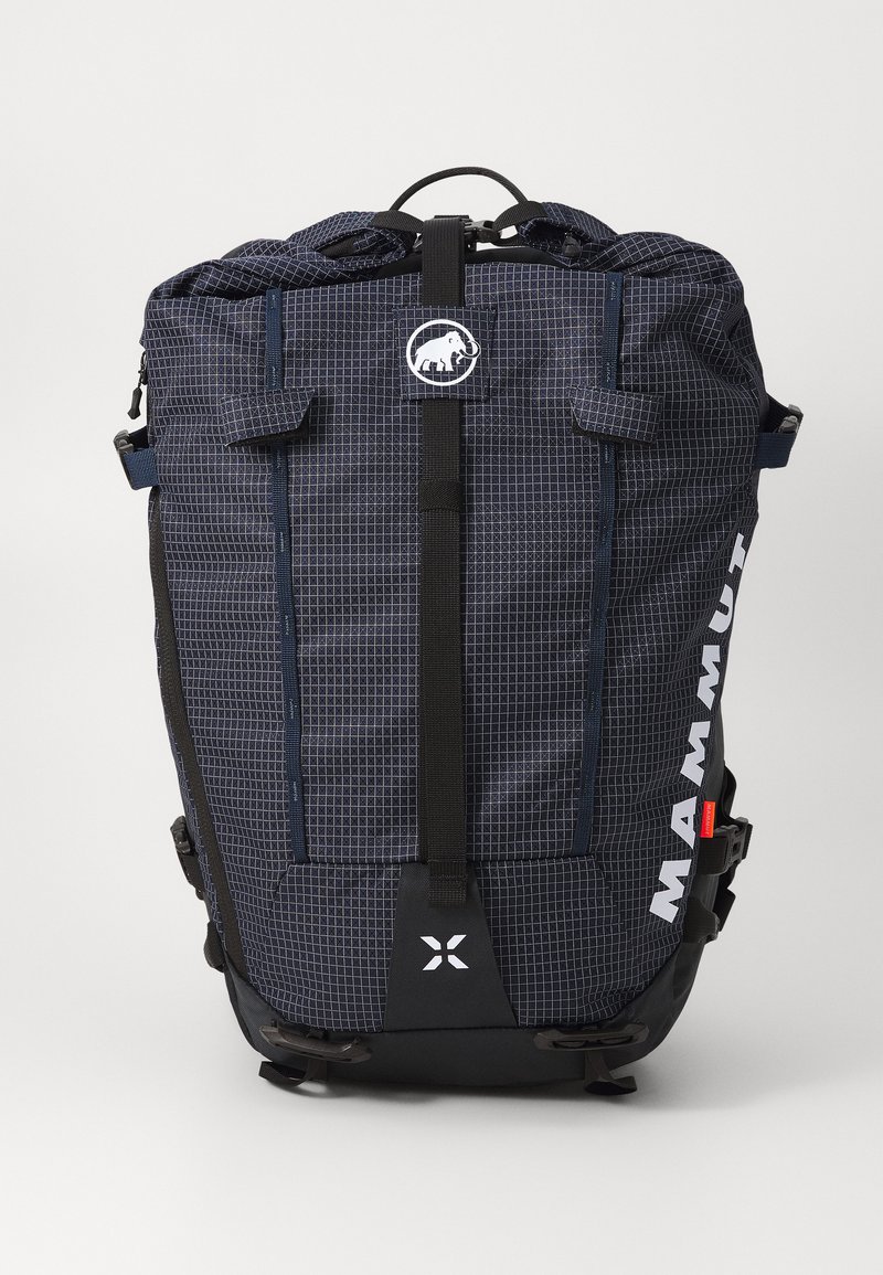 Tumši zila mugursoma ar režģa rakstu, melniem akcentiem, augšējo rokturi, regulējamiem siksnām, priekšējo logo un sānu sprādzēm drošai aizvēršanai.