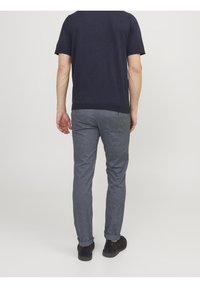 Marinblå bomulls-t-shirt med korta ärmar, kombinerad med ljusgrå byxor. Byxorna har en slim fit och uppvikta fållar. Svarta skor fullbordar outfiten.