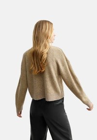 Maglione lavorato a maglia in una tonalità oro chiaro con una silhouette corta, maniche larghe e una texture morbida, abbinato a pantaloni neri.