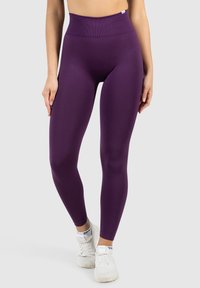 Lila High-Waist-Leggings aus elastischem Stoff, mit einer glatten Textur und einer figurbetonten Silhouette, kombiniert mit weißen Sportschuhen.