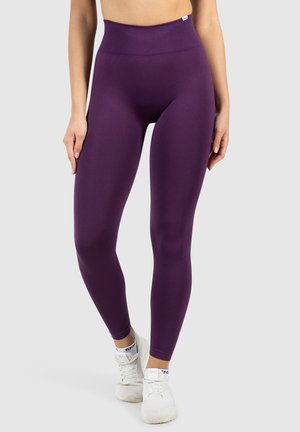Paarse high-waisted leggings van rekbaar materiaal, met een gladde textuur en een getailleerde silhoutte, gecombineerd met witte sportschoenen.