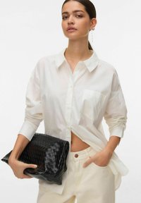 Chemise blanche à boutons avec manches longues et une poche avant, associée à une pochette noire tressée. Le tissu semble lisse, design structuré.