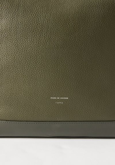 Mala verde em couro com um acabamento texturizado. Apresenta um destaque liso de um verde escuro na base e texto de marca em prata exibido em destaque.