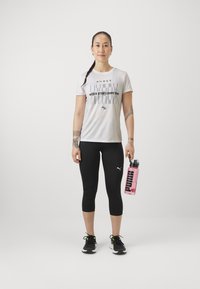 Valge sportlik T-särk musta tekstiga, mustad retuusid ja mustad jooksujalatsid. Hoia roosa veepudelit, millel on 'PUMA' logo. Kitsas lõike disain.