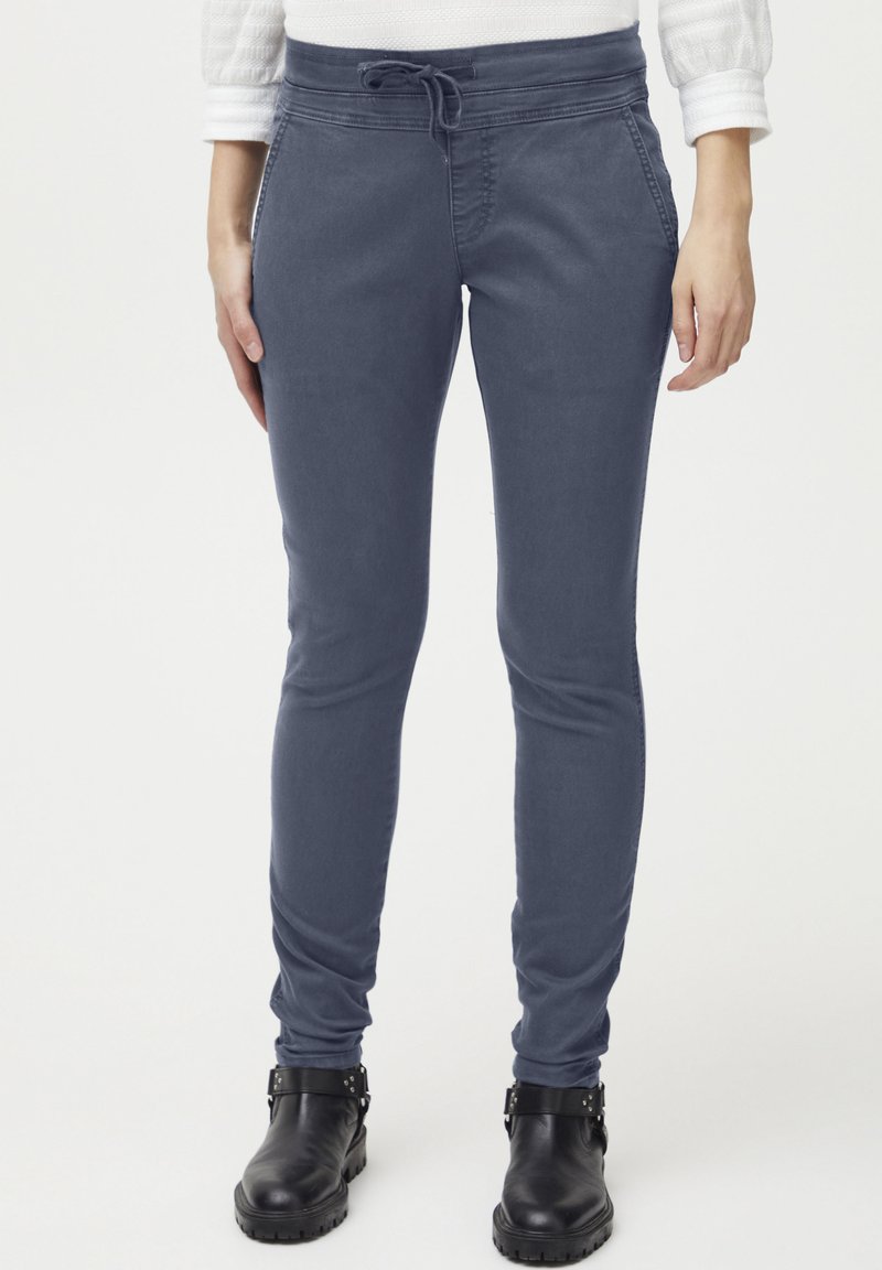 Pantalones jogger de algodón elástico en azul con cintura ajustable y diseño slim-fit, complementados con botas de tobillo negras.