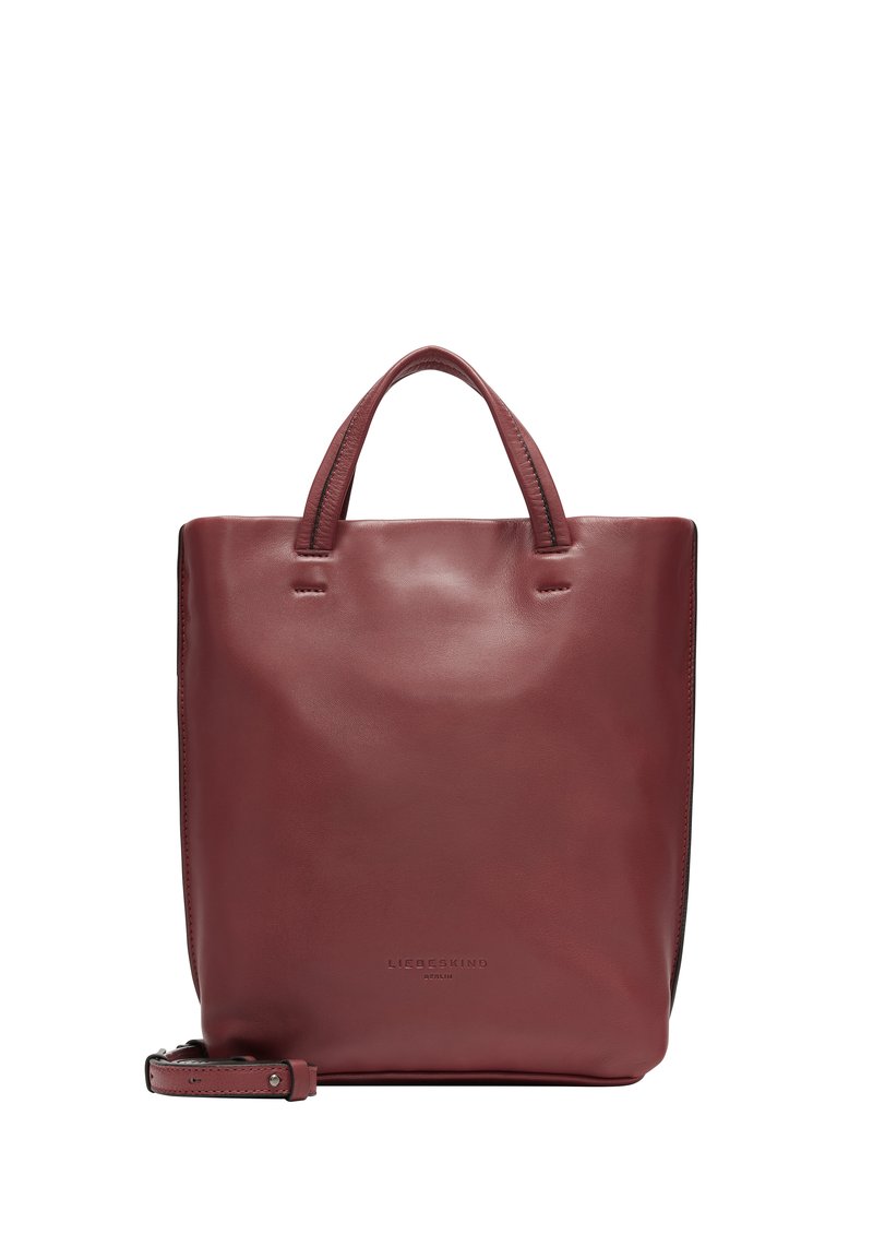 Sac rectangulaire en cuir bordeaux avec deux courtes poignées, couture minimale et une bandoulière amovible. Nom de la marque embossé à l'avant.