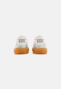 Schwere Sneaker mit einem weißen und grauen Obermaterial, pinken Akzenten an der Ferse und transparenten orangen Gummisohlen; das Branding "SCOTCH & SODA" ist sichtbar.