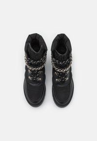 Botas de tobillo acolchadas negras con un upper texturizado tipo calcetín, acento de cadena de metal y cordones gruesos. Suela de goma con capucha de toe reforzada.