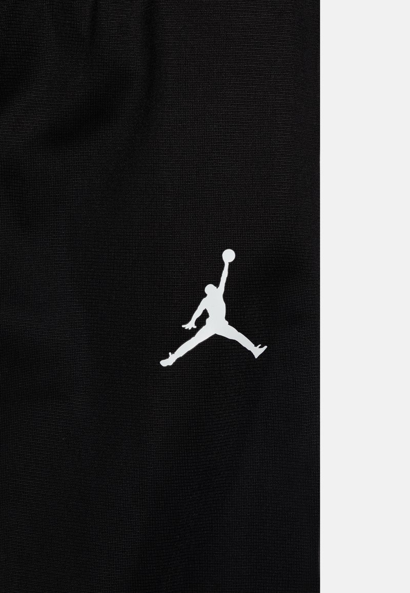 Un tejido negro con una textura suave presenta un logo Jumpman blanco en una postura dinámica, que muestra un movimiento atlético.