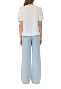 Blusa bianca con maniche a sbuffo e scollatura rotonda classica, abbinata a jeans a gamba larga blu chiaro, entrambi con texture morbide e lisce.
