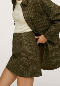 Jupe à motifs marron et veste oversize avec des boutons noirs. Le tissu a un aspect texturé, présentant un design complexe sur toute la surface.