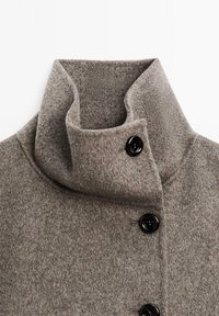 Cappotto di lana grigio con colletto alto, due bottoni neri e un tessuto morbido e lavorato. Design semplice e sartoriale senza ulteriori motivi.