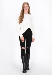 Hvid, fluffet striktrøje med et afslappet silhuet, parret med sorte, slidte skinny jeans og knæhøje sorte støvler.