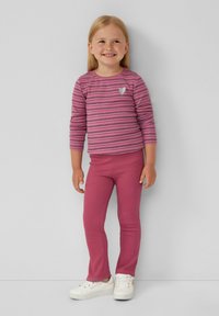 Roze gestreepte blouse met lange mouwen en een klein hartdetail, gecombineerd met effen roze geribde leggings. Witte sneakers maken de outfit af.
