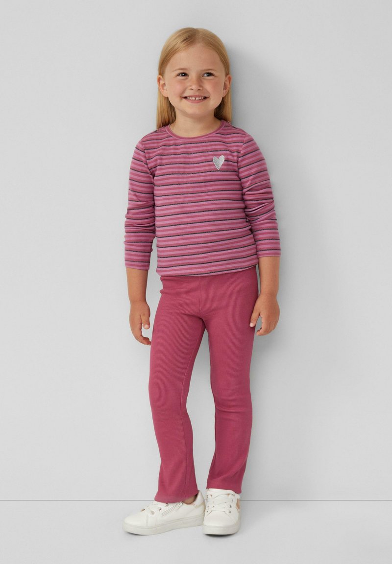 Roze gestreepte blouse met lange mouwen en een klein hartdetail, gecombineerd met effen roze geribde leggings. Witte sneakers maken de outfit af.