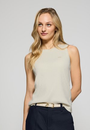 Top sin mangas de canalé en color beige claro con un cuello redondo, combinado con pantalones oscuros y un cinturón blanco con un detalle de hebilla dorada.