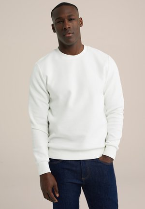 Sudadera blanca texturizada con cuello redondo y puños acanalados, combinada con jeans oscuros. La tela parece suave y transpirable.