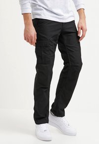 Svarta cargobyxor i bomull, med flera fickor, rak passform och en mjuk yta, kombinerade med vita sneakers.