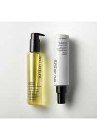 Due prodotti per la cura dei capelli: una bottiglia trasparente gialla con un erogatore nero etichettata "Essence Absolue" e una bottiglia spray bianca con un ugello nero.