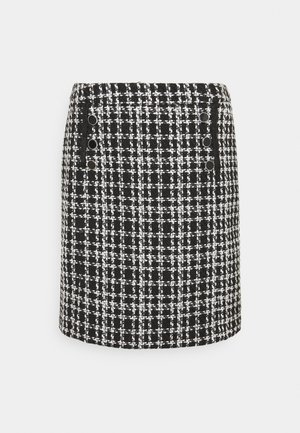 Mini-jupe en tweed à carreaux noir et blanc avec six boutons noirs en deux rangées verticales à l’avant.